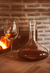 Decanter and wine glass on wooden table against fireplace
