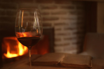 Glass of red wine and blurred fireplace on background