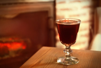 Glass of mulled wine on wooden table against blurred fireplace