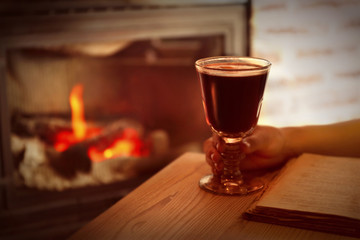 Female hand and glass of mulled wine with blurred fireplace on background
