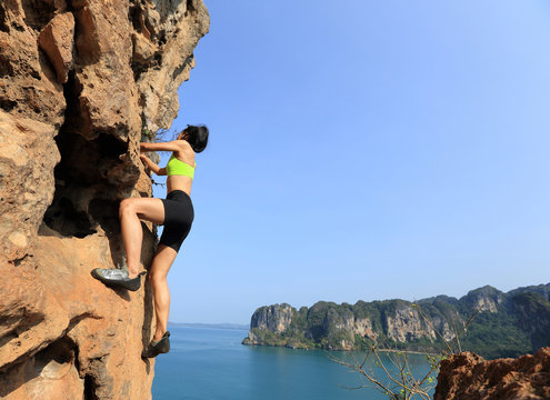 young woman rock climber climbing at seaside cliff