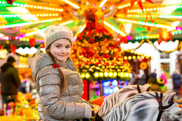 Portrait of a happy little girl riding on horses on carousel, tr