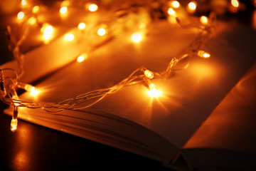 Open book and beautiful garland on table, closeup