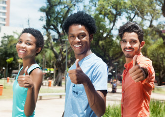 Group of three latin american young adults showing thumbs in city