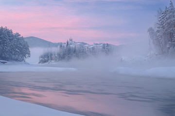 Castle/The hotel, which stands on the bank of a frozen river, half hidden in mist from the river....