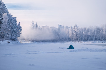 Imperial fishing/Fisherman on the frozen river took refuge tent. Winter fishing on the river Katun in front of the hotel like the old castle. Katun River, Mountain Altai, Siberia, Russia
