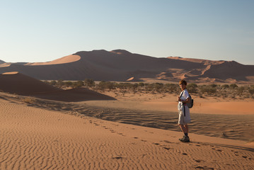 Fototapeta na wymiar Tourist walking on the scenic dunes of Sossusvlei, Namib desert, Namib Naukluft National Park, Namibia. Afternoon light. Adventure and exploration in Africa.