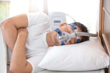 Man sleeping in bed wearing CPAP mask ,sleep apnea therapy.Happy and healthy senior man sleeping...