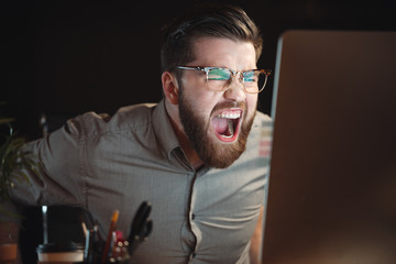 Bearded designer working with computer late at night and screaming.