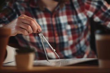Cropped picture of designer working at night and holding compasses