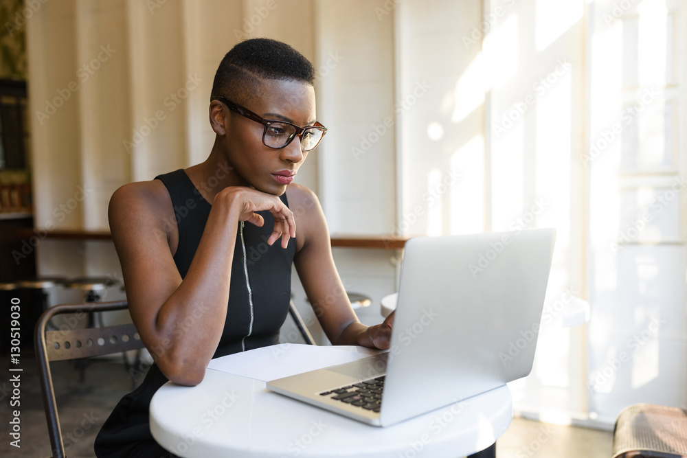 Wall mural young fashionable african business woman working hard at the cafe on the laptop