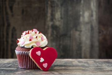 Valentine cupcake and cookie with heart shape decorated with sweet hearts on wooden table
