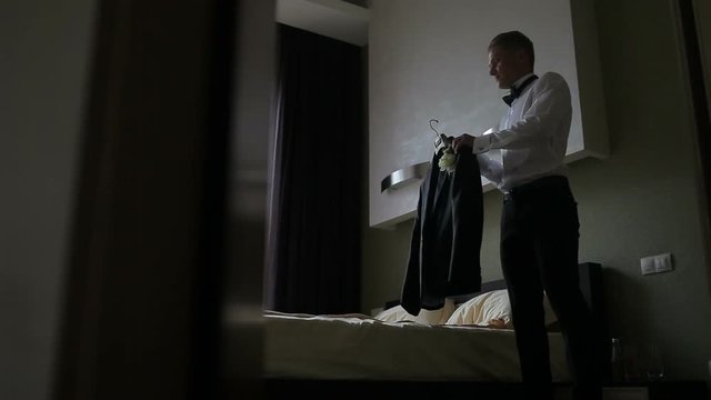 Young man takes off hangers his jacket in light room. Stylish man in a fashion suit costume preparing to go out at a reception or wedding. 
