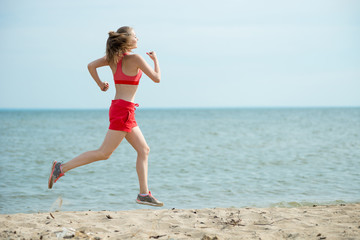 Young lady running. Woman runner running at the sunny summer sand beach. Workout near ocean sea coast. Beautiful fit girl. Fitness model caucasian ethnicity outdoors. Weight loss exercise. Jogging.