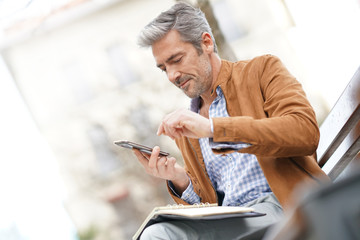 Businessman sitting on public bench, scheduling working day
