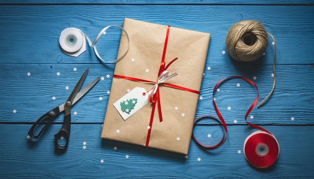 Gift packing handmade paper and red ribbon on blue wooden boards with white snowflakes