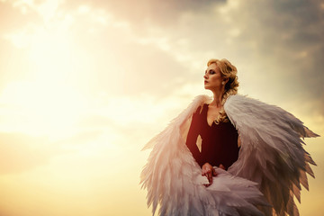 Young glamorous woman in a black dress with a large white angel wings on the background of a...