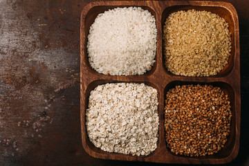 Raw sushi rice, brown rice, bulgur and buck wheat in a wooden bowl on dark background