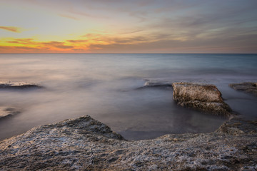 Fototapeta na wymiar Rocks surrounded by silky waves water after a vivid sunset