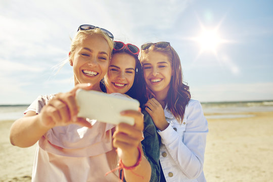 group of smiling women taking selfie on beach