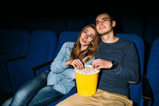 Cinema date, happy young couple with popcorn watching romantic movie in cinema.