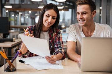 Coworkers sit by the table with documents and laptop