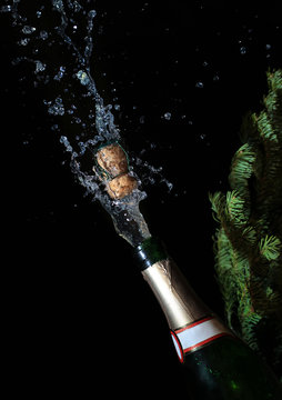 Bottle of Champagne with popping cork and spray on bla