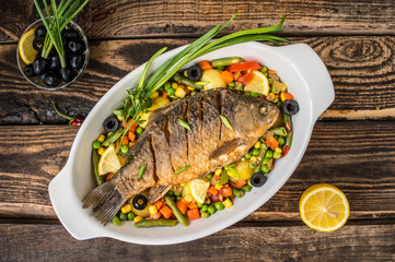 Grilled fish on brown plate with herbs and lemon  old wooden background, top view. Mediterranean luxurious seafood concept.