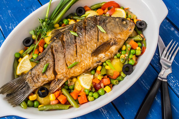 Grilled fish on brown plate with herbs and lemon  old wooden background, top view. Mediterranean luxurious seafood concept.