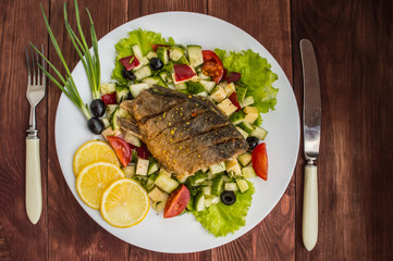 Fried fish fillet on a bed of Caesar salad. Wooden background. Top view.