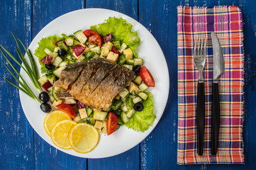 Fried fish fillet on a bed of Caesar salad. Wooden background. Top view.