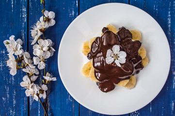 Bananas covered with chocolate on a white plate. Top view