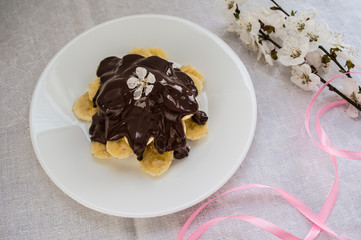 Bananas covered with chocolate on a white plate. Top view