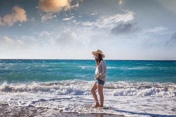 Young woman in a hat walking along the seashore. Holidays and tr
