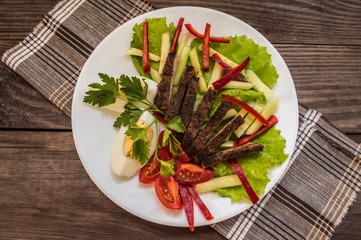 Salad of roasted meat, lettuce, boiled eggs, paprika, tomato and cucumber on a wooden table. Top view
