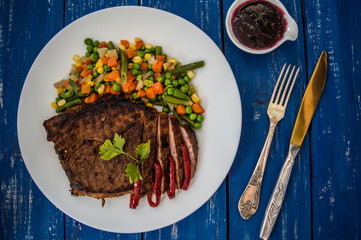 Grilled steak with steamed vegetables on a white plate. blue table. Top view