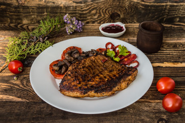 Grilled steak with mushrooms, tomatoes and peppers on a white plate. Wooden background