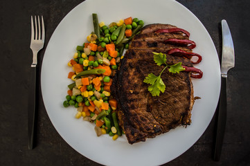 Grilled steak with steamed vegetables on a white plate. old table. Top view