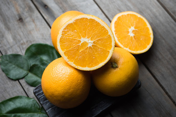 Macro view of vibrant, yellow lemon slice and two whole lemons on dark brown, rustic, wooden table