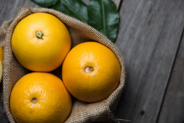 Macro view of vibrant, yellow lemon slice and two whole lemons on dark brown, rustic, wooden table