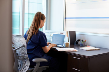 Nurse Wearing Scrubs Working At Desk In Office