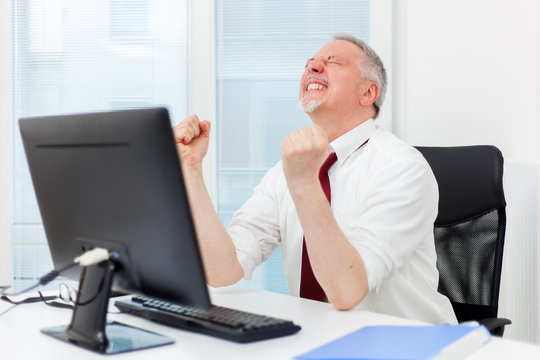 Mature businessman raising arms in front of his pc