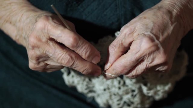 93-year-old woman sits at couch and knits lace napkin. Hands closeup.