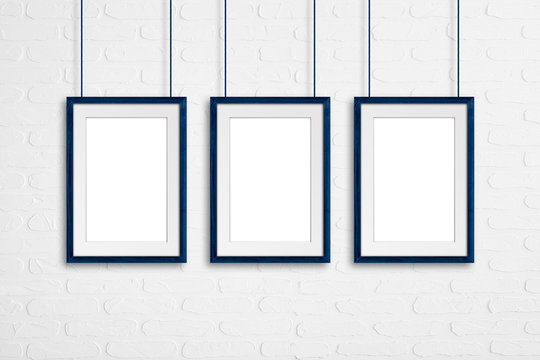 Blue  wooden frames, hanging on cords against white bricks wall, interior decor mock up