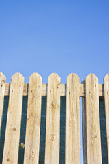 Detail of a wooden fence built with spiky wooden boards against a blue sky