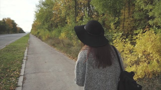 Young pretty woman in black hat and glasses walking down the autumn street HD