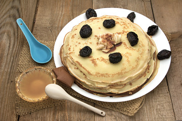 Pancakes with berries, fruits, chocolate, pine nuts and honey on white plate on a natural wooden board