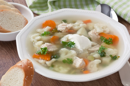 Soup with chicken, cauliflower, vegetable and bread in white plate / Vegetable soup with chicken, cauliflower, carrot, potato, parsley, cream and slice white bread in plate on wooden background