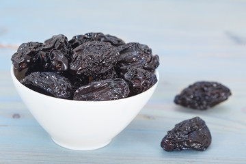Dry plums or prunes in white bowl over blue background