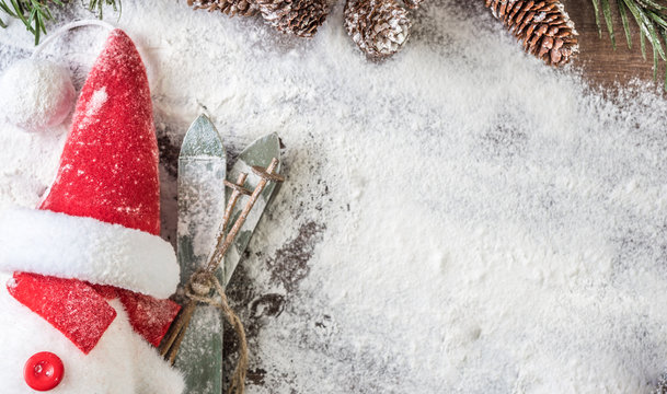 Snowman Undercover As Santa Claus With An Oversize Red Hat And A Pair Of Wood Skis On A Snowy Backgound